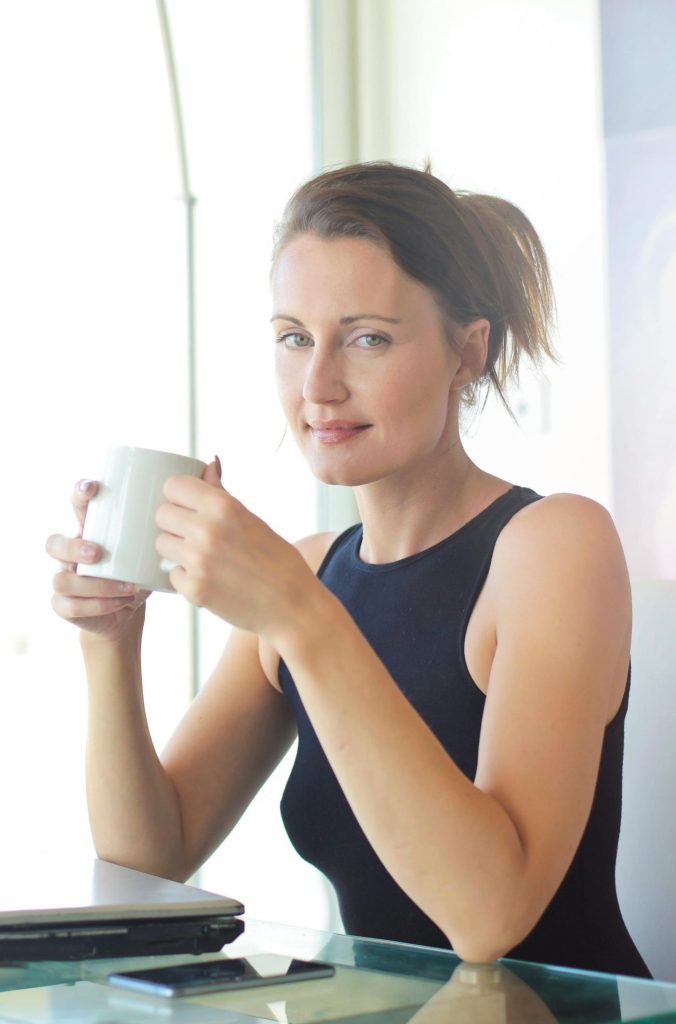 Young woman sitting at her desk, holding a coffee cup and smiling. Ideal for workplace and lifestyle themes.